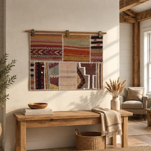 May include: A rectangular wall hanging composed of multiple stitched fabric panels featuring diverse geometric patterns and a color palette of red, orange, yellow, brown, and cream. The textile is suspended from a wooden rod by three metal clips.