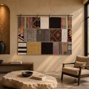 Puede incluir: Un tapiz rectangular para pared compuesto por varios parches de tela cosidos en diversos colores, incluyendo negro, blanco, amarillo y rojo, con patrones geométricos, rayas y texturas sólidas, suspendido de una barra metálica con clips.