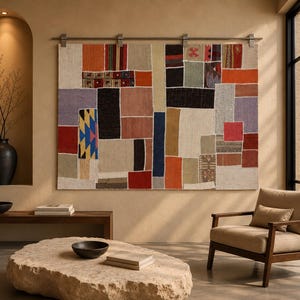 May include: A large rectangular wall hanging composed of various fabric patches in diverse colors including orange, red, blue, black, and beige. The textile piece is mounted on a horizontal metal rod with clips, displaying a geometric patchwork design.
