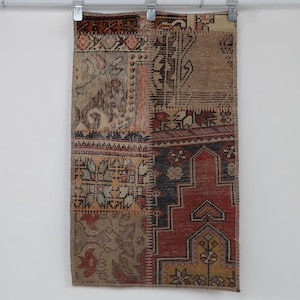 Puede incluir: Una alfombra de retazos rectangular que presenta una variedad de segmentos textiles tejidos en tonos apagados de rojo, azul, marrón y beige. La alfombra muestra diversos patrones geométricos y florales cosidos juntos, creando una superficie texturizada.