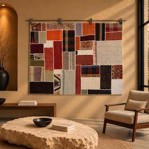 May include: A large rectangular wall hanging featuring a patchwork design composed of various fabric swatches in shades of red, orange, brown, black, white, and grey, suspended from a metal rod with four clips attached to the top edge.