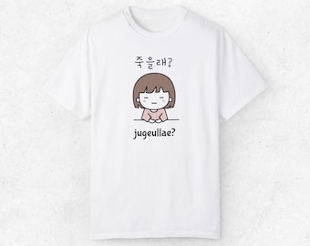 May include: White t-shirt with a cartoon illustration of a girl with brown hair and a pink shirt. The text "주을래?" is above the illustration and "jugeullae?" is below the illustration.