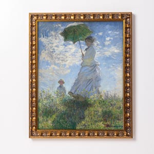 May include: A framed painting of a woman in a white dress holding a green umbrella, walking in a field with a child. The sky is blue with white clouds. The painting is in a gold frame.