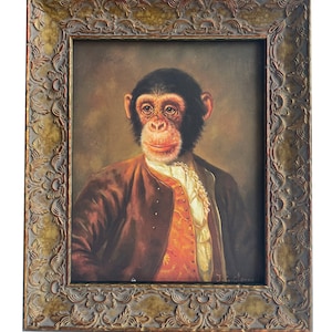 May include: A framed painting of a chimpanzee dressed in a brown jacket, orange waistcoat, and white shirt with a lace collar. The chimpanzee is looking directly at the viewer with a serious expression. The painting is in a gold-coloured frame with ornate details.