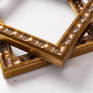May include: Two ornate gold picture frames with a decorative, raised, wavy design on the edges. The frames are stacked on top of each other.