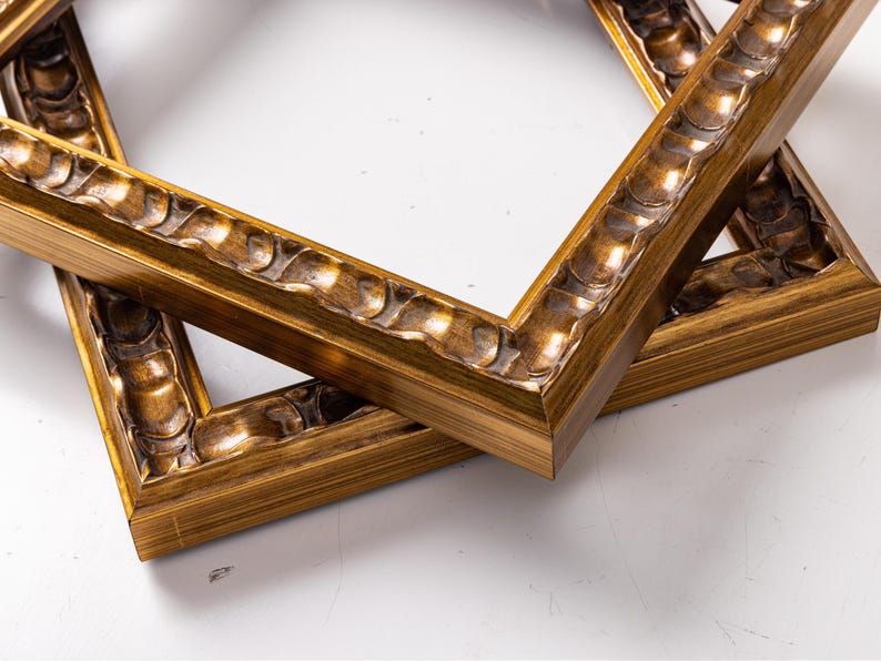 May include: Two ornate gold picture frames with a decorative, raised, wavy design on the edges. The frames are stacked on top of each other.