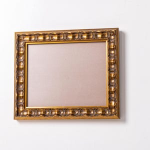 May include: A gold-colored picture frame with a decorative, ornate border. The frame is empty and ready to display a photo or artwork.