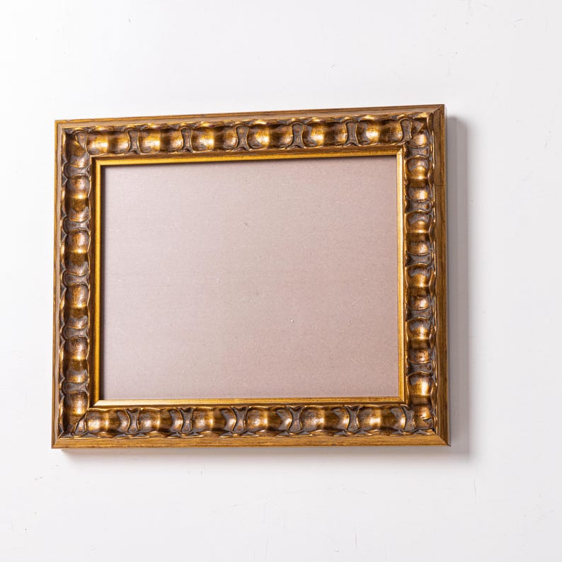 May include: A gold-colored picture frame with a decorative, ornate border. The frame is empty and ready to display a photo or artwork.