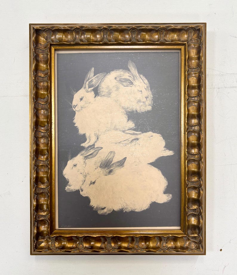 May include: A framed print of a black and white illustration of four white rabbits stacked on top of each other. The rabbits are depicted in a realistic style with detailed fur and whiskers. The print is framed in a gold-colored frame with a decorative border.