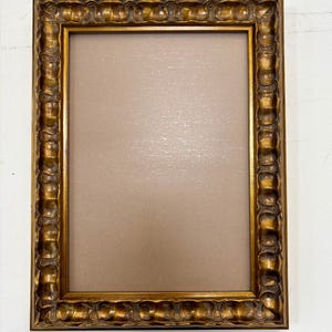 May include: A gold picture frame with a decorative, ornate design. The frame is empty and ready to display a photo or artwork.