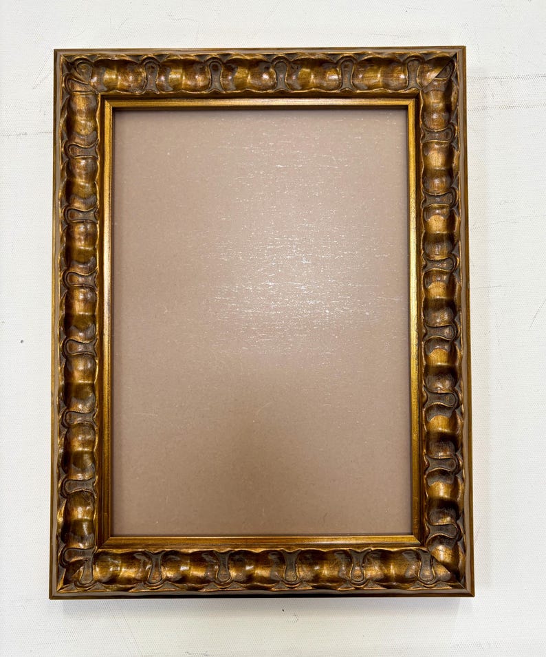 May include: A gold picture frame with a decorative, ornate design. The frame is empty and ready to display a photo or artwork.