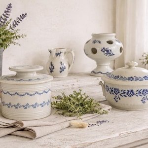 Könnte beinhalten: Eine Sammlung von Küchengeschirr aus Keramik im Vintage-Stil mit blauen Blumenmustern. Enthält eine Butterdose, eine Auflaufform mit Deckel, eine dekorative Vase und einen kleinen Krug. Die Artikel sind auf einer weißen Holzoberfläche angeordnet.