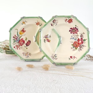 Peut inclure: Deux assiettes octogonales crème avec des motifs floraux et une bordure verte. L'une des assiettes a une poignée. Une pile d'assiettes similaires est visible en arrière-plan. Les assiettes présentent des fleurs rouges, jaunes et bleues.