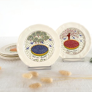 Puede incluir: Un juego de platos de cerámica color crema con bordes festoneados. Dos platos están de pie, uno con una ilustración de tarta de arándanos con el texto Tarte aux Myrtilles, y el otro de tarta de cerezas con el texto Tarte aux Cerises.