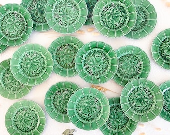 May include: A collection of round green ceramic plates featuring a raised relief pattern of grape leaves and clusters of grapes. Each plate has a scalloped edge and a glossy finish, arranged in a scattered layout across the frame.