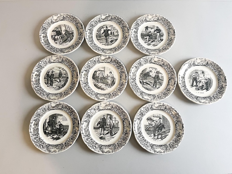 K&ouml;nnte beinhalten: Set aus zehn wei&szlig;en Keramiktellern mit Schwarzwei&szlig;illustrationen von Personen in verschiedenen Szenen. Die Teller haben einen dekorativen Rand.