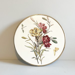 Könnte beinhalten: Ein weißer Keramikteller mit goldfarbenem Rand zeigt ein gemaltes Blumenmuster aus rosa, gelben und roten Nelken mit grünen Blättern und einem gelben Schmetterling.