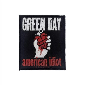 May include: A rectangular black embroidered patch featuring the white text GREEN DAY at the top and red text american idiot at the bottom. In the center is a white hand holding a red heart-shaped grenade with black grid lines and dripping red.