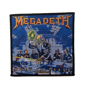 Puede incluir: Un parche bordado cuadrado con el logotipo de Megadeth en naranja y amarillo en la parte superior. El diseño muestra un esqueleto con traje sosteniendo un objeto verde brillante, rodeado de figuras con traje. El texto RUST IN PEACE está abajo.