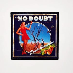 Könnte beinhalten: Quadratischer Aufnäher mit marineblauem Hintergrund und dem Text "NO DOUBT" oben. Der Aufnäher hat ein rundes Bild einer Frau in einem roten Kleid, einem Baum und den Worten "Tragic Kingdom".