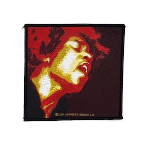 Può includere: Una toppa ricamata quadrata raffigurante un ritratto stilizzato di Jimi Hendrix nei toni del rosso, giallo e bianco su sfondo scuro. Il bordo inferiore include il testo ©2019 AUTHENTIC HENDRIX LLC in piccole lettere gialle.