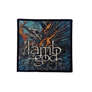 Puede incluir: Un parche tejido cuadrado con una ilustración oscura y detallada de un cráneo de ave rodeado de llamas naranjas y texturas azules. El texto "lamb of god" está centrado en blanco, con "OMENS" debajo y "©2022 LAMB OF GOD" en el borde inferior.