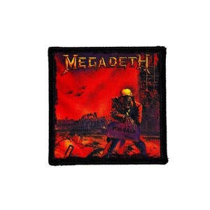 Op de afbeelding: Vierkante patch met een zwarte rand met de bandnaam "MEGADETH" in gouden letters. De afbeelding toont een figuur die een "FOR SALE" bord vasthoudt tegen een rode en oranje achtergrond met een stadsgezicht.
