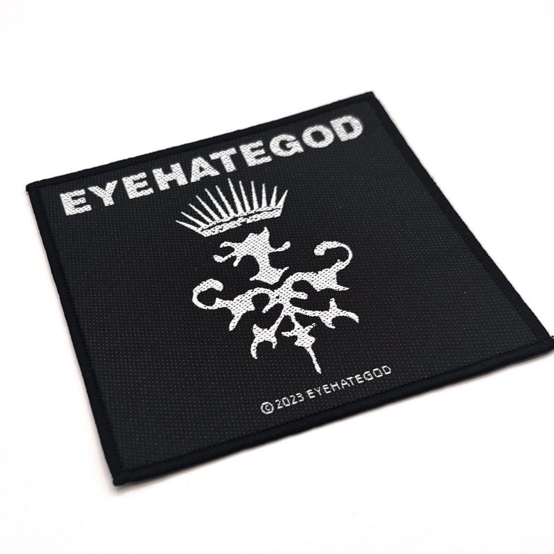 May include: A square black patch featuring white text and a white emblem. The text "EYEHATEGOD" is at the top, with a crown above a stylized design. The text "&copy; 2023 EYEHATEGOD" is at the bottom.