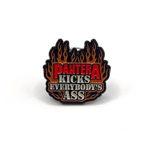 May include: A black and red enamel pin featuring the text "PANTERA KICKS EVERYBODY'S ASS" within a flame design. This pin is a collectible item, possibly for fans of the band Pantera.