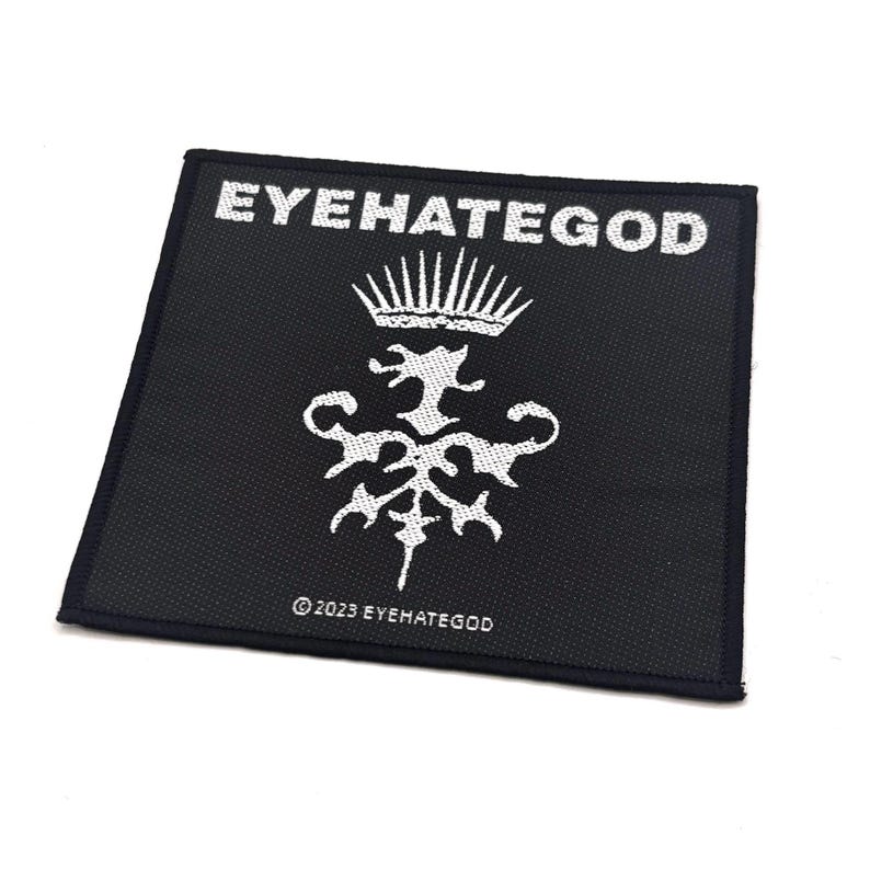 May include: A square black patch featuring white text and a detailed emblem. The words "EYEHATEGOD" are at the top, with an intricate design beneath. The copyright notice "&copy; 2023 EYEHATEGOD" is at the bottom.