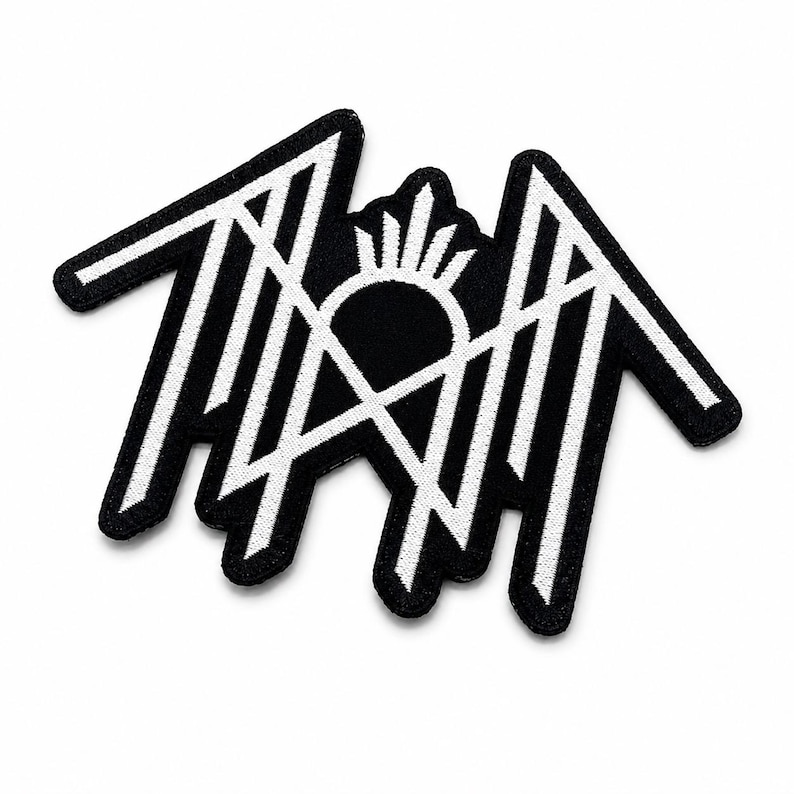 May include: A black and white embroidered patch featuring a stylized, angular geometric design. The graphic consists of sharp, interconnected lines forming a symmetrical shape with a central sunburst element, all outlined in a thick black border.