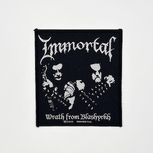 Könnte beinhalten: Schwarzer quadratischer Aufnäher mit dem Bandnamen "Immortal" in weißer gotischer Schrift. Der Aufnäher zeigt zwei stilisierte Figuren und den Text "Wrath from Blashyrkh". Ein Accessoire zum Thema Musik.
