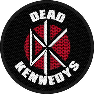 Peut inclure: Un écusson rond noir avec les mots "DEAD KENNEDYS" en blanc, incurvés autour d'un motif central. Le motif comprend un cercle rouge en forme de brique avec des lignes blanches qui l'intersectent. L'écusson a un aspect texturé.
