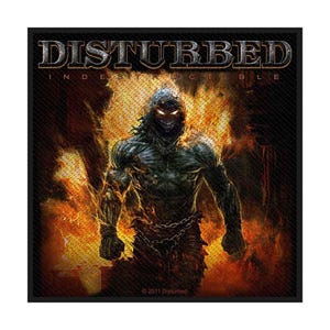 May include: Black square patch with the band name "DISTURBED" and the word "INDESTRUCTIBLE". The image shows a muscular, dark figure with glowing eyes and flames. The figure is chained, set against a fiery backdrop.