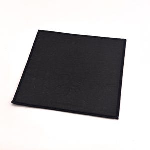 May include: A square, black coaster with a textured surface and a stitched border. The coaster is designed to protect surfaces from heat and moisture. The dark colour and simple design make it suitable for various decor styles.