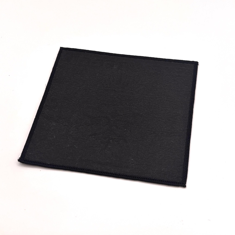 May include: A square, black coaster with a textured surface and a stitched border. The coaster is designed to protect surfaces from heat and moisture. The dark colour and simple design make it suitable for various decor styles.