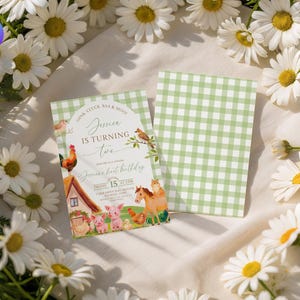 May include: A farm-themed invitation with the text "Jessica is Turning Two" and farm animals. The invitation has a green gingham pattern on the back. White daisies surround the invitation on a white fabric background.