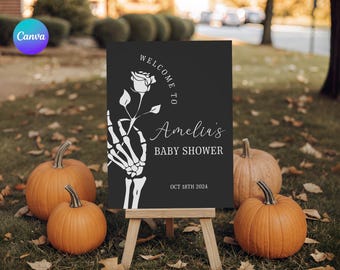 May include: A black baby shower sign with white text and a skeleton hand holding a rose. The sign reads "Welcome to Amelia's Baby Shower, Oct 18th 2024." Orange pumpkins surround the sign.