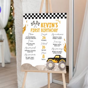 May include: A birthday sign on an easel with the text "Kevin's First Birthday." The sign includes a monster truck graphic and details about the birthday celebrant, such as height, weight, and favorite things. The sign is decorated with flames and checkered flags.