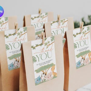 Könnte beinhalten: Geschenktüten aus Kraftpapier mit "Thank You" Anhängern. Die Anhänger zeigen eine Safari-Tierillustration und den Text "So much for showering our little baby". Jeder Anhänger wird von einer Holzklammer gehalten.