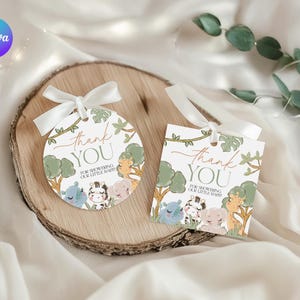 May include: Two baby shower gift tags with a safari animal theme. One tag is round, the other rectangular. Both have a white ribbon and the words "Thank You" in script. The tags feature illustrations of a giraffe, zebra, elephant, and hippo.