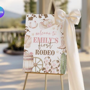 May include: A welcome sign for "Emily's First Rodeo" features a cowboy theme with a hat, boots, and horseshoe illustrations. The sign is on a gold easel, with a large white bow and fabric draped on the side. The sign's color palette includes pink, brown, and white.
