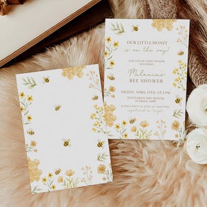 Op de afbeelding: Een baby shower uitnodiging met een aquarel ontwerp van gele honingraat, bloemen en bijen. De tekst luidt "Onze kleine honing is onderweg!" en "Melanin's Bijen Shower". De uitnodiging bevat de datum, tijd en locatie van de shower.