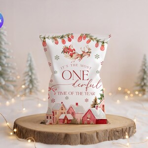 May include: A white gift bag with a Christmas theme. The bag features illustrations of Santa Claus in a sleigh, houses, snowflakes, and the text "It's the most ONE derful TIME OF THE YEAR."