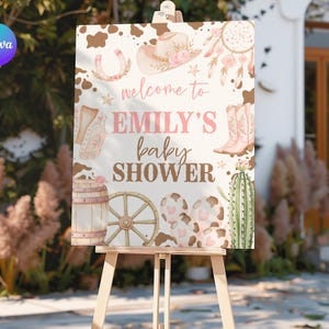 May include: A wooden easel displays a baby shower sign with a western theme. The sign features illustrations of a cowboy hat, boots, and a horseshoe, with the text "Welcome to Emily's Baby Shower" in pink and brown.