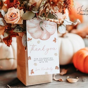 May include: A fall-themed arrangement featuring a bouquet of flowers, pumpkins, and a 'Thank You' tag. The tag has a pumpkin illustration and the text: 'Thank you for celebrating my first birthday with me'. The tag measures 2x3.5 inches.