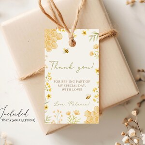 May include: A thank you tag with a bee and honeycomb design. The tag is white with yellow flowers and green leaves. The text on the tag reads "Thank you! For bee-ing part of my special day. With love! Love, Melanin".