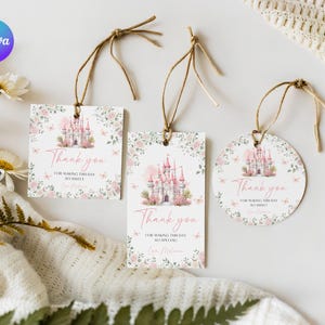 May include: Three gift tags with a pink castle design and the words "Thank you". The tags are rectangular and circular, with floral accents and attached with twine. The background is white.