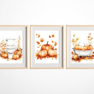 Puede incluir: Tres pinturas de acuarela enmarcadas con un tema otoñal. La primera pintura muestra un inodoro con calabazas y hojas de otoño. La segunda pintura muestra un grupo de calabazas con hojas de otoño. La tercera pintura muestra una bañera con calabazas y hojas de otoño.