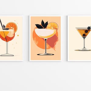 May include: Three printable art prints featuring illustrations of cocktails. The first print shows an orange and red cocktail with a slice of orange. The second print shows a white cocktail with a slice of orange and green leaves. The third print shows a brown cocktail with two olives.
